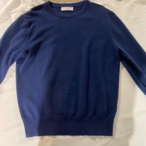 Mörkblå kashmirtröja från Carmes - Säljer en klassisk mörkblå rundhalsad tröja från Carmes i mjuk kashmir. Tröjan har långa ärmar och ribbade muddar vid ärmslut, hals och nederkant. Perfekt för lager-på-lager och stilrena outfits.