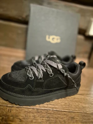 Ugg lowmel lo OANVÄND! - Säljer ett par svarta UGG sneakers med chunky platt sula och breda grå snören med mönster. Ovandelen är i mocka och mesh för extra komfort och stil. UGG-logga på plösen och insidan. Perfekt för dig som gillar streetwear och vill ha något som sticker ut.Helt oanvända bara provade box och kvitto finns kvar.
