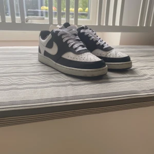 Nike Court Vision svartvita sneakers - Svartvita Nike Court Vision sneakers med klassisk design, vit sula och svarta detaljer. Skorna har snörning, rund tå och är tillverkade i syntet och skinn. Perfekta för dig som gillar en clean och sportig look. Ny pris 1000/800kr 