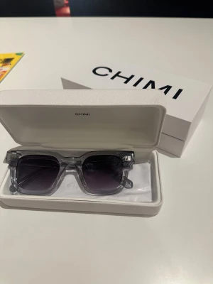 Gråa solglasögon från CHIMI - Snygga svarta solglasögon från CHIMI med klassisk form. Kommer i original vit hård box och fodral med CHIMI-logga. Perfekta för att lyfta din stil och skydda ögonen mot solen.