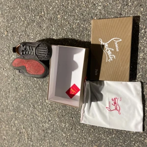 Christian Louboutin svarta sneakers med nitar - Svarta sneakers från Christian Louboutin med coola nitar på tån och den ikoniska röda sulan. Skorna har snörning och är tillverkade i mocka och skinn. Kommer med originalkartong och dustbag. Perfekta för dig som vill sticka ut med lyxig streetstyle.