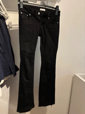 Svarta bootcut jeans från Gina Tricot - Svarta jeans från Gina Tricot, modell Perfect Jeans, med bootcut passform i strl 38. Jeansen har silverfärgade knappar och råa kanter vid bensluten för en edgy vibe. Dom är alltså lite längre eftersom att jag har sprättat upp de. Materialet är stretchigt jeans och midjan är normal. De är endast använda en gång så mycket bra skick om man tänker bort benslutet.