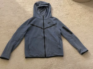 Blå Nike Tech Fleece hoodie - Nike Tech Fleece hoodie i blått, storlek 147-158 cm. Blixtlåset har tappat lite färg men syns ej när man har på sig den.