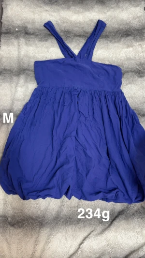 Blå kort klänning med axelband - Snygg blå kort klänning med breda korsade axelband och voluminös kjol. Perfekt för varma dagar och enkel att styla med sneakers eller sandaler. Luftigt material och avslappnad passform för en chill vibe.🌸 Fint använt skick. Storlek M