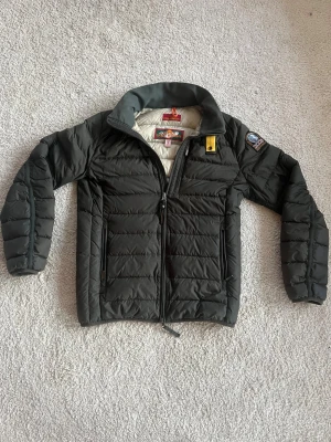 Svart dunjacka från Parajumpers  - Säljer en svart dunjacka från Parajumpers Super Lightweight i storlek S. Jackan har quiltad design, hög krage med grå insida, gul detalj vid halsen och patch på ärmen. Två dragkedjefickor och hel dragkedja framtill. Perfekt för kalla dagar.