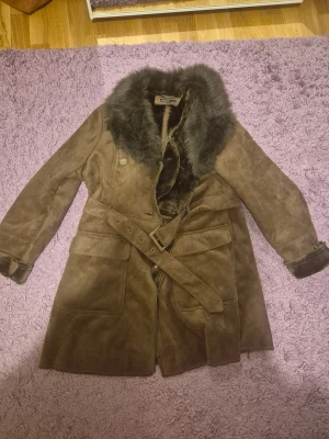 Brun kappa från KappAhl - Snygg brun pälsjacka från KappAhl med fluffig krage och muddar i mörkbrun päls. Jackan har bälte i midjan, stora fickor och knappar vid ärmslut. Materialet är mocka med pälsdetaljer, perfekt för kalla dagar. Priset kan diskuteras 💕💐 har haft länge men aldrig använts. Medföljer en extra knapp 