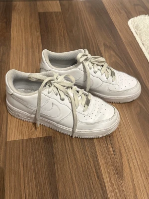 Nike Air Force 1 vita sneakers - Fräscha Nike Air Force 1 sneakers i helvitt skinn med klassisk rund tå och platt sula. Modellen har perforerade detaljer på tån för extra ventilation och snörning framtill. Snygg och tidlös design som passar till allt. Storlek 39.