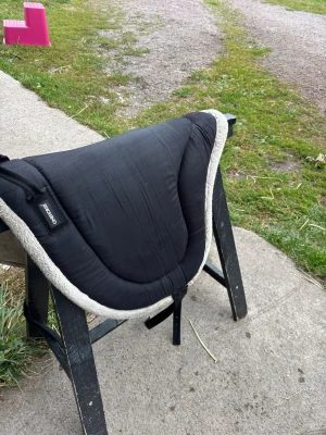 Svart ridpad från one horse - Säljer en svart ridpad från Acavallo med mjuk, ljusgrå kant i fuskpäls. Snygg, ergonomisk form som ger bra komfort för både ryttare och häst. Perfekt för barbackaridning och har praktiska remmar för enkel fastsättning.