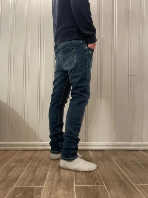 Blåa dondup jeans - Snygga blå dondup jeans med avslappnad fit och klassisk femficksdesign. Jeansen har en mörk tvätt med lätt slitning framtill och detaljerade sömmar på bakfickorna. Materialet är stretchigt jeans för skön passform och rörelsefrihet.