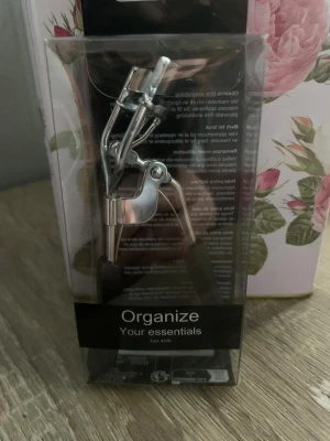 Ögonfransböjare i metall - Snygg ögonfransböjare i silverfärgad metall med svarta handtag för extra grepp. Perfekt för att få till den där fina böjen på fransarna. Kommer i originalförpackning och är enkel att använda för ett lyft till din sminkrutin.