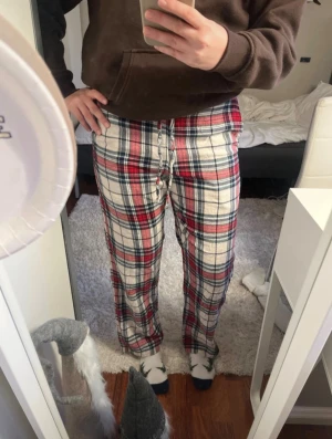 Julig mjukisbyxa med snöre  - Säljer ett par rutiga mjukisbyxor i rött, svart och vitt/beige med snörning i midjan. Byxorna har en loose passform och är perfekta för att hänga hemma eller mysa. Materialet är mjukt och skönt, och mönstret är klassiskt rutigt. Passar S.