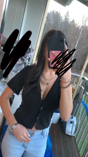 Svart croppad blus från 157 XS - Svart blus från 157 i croppad modell med korta ärmar och v-ringad hals. Toppen har två snygga knappar framtill och är gjord i mjukt bomullsmaterial. Perfekt för dig som gillar enkel och stilren design 🩷🩷