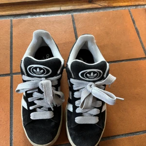 Adidas Campus svarta sneakers mocka - Svarta Adidas Campus sneakers i mocka med vita detaljer och klassiska tre ränder på sidan. Har inte använt mycket. Finns även svarta skosnören till. 