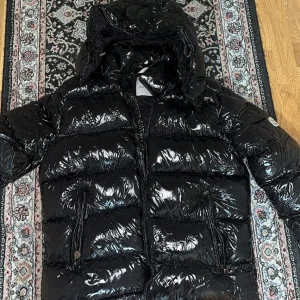 Svart Moncler pufferjacka med huva - Helt ny Moncler-jacka, fick den i födelsedagspresent. Tror inte jag kommer använda den, så lägger ut den här istället. QR-koden fungerar och man kan även skanna loggan på armen med mobilen för att se att den är äkta (dock utan kvitto).