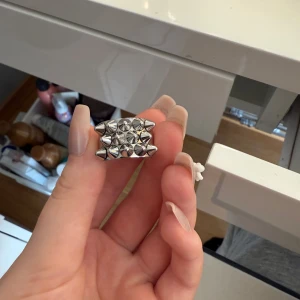 Silvrig ring med nitar från Edblad - Cool silvrig ring från Edblad med flera spetsiga nitar på ovansidan som ger en edgy vibe. Ringen är i metall och har en bred form som sticker ut. Perfekt för dig som gillar att addera lite attityd till din stil.