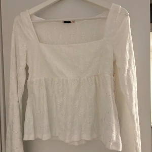 Helt oanvänd vit blus med broderade detaljer Nelly - Superfin oanvänd vit blus från Nelly med lång ärm och fyrkantig ringning. Blusen har broderade blommönster i tyget och en lätt volang nedtill. Perfekt för dig som gillar romantisk och feminin stil. Tillverkad i bomull för en luftig känsla.