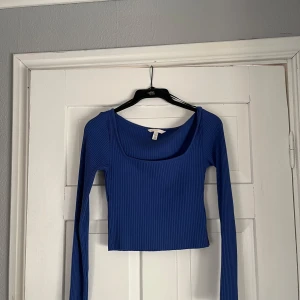 Blå ribbad långärmad topp H&M - Snygg blå croppad topp från H&M med ribbad struktur och lång ärm. Toppen har en fyrkantig urringning framtill och är figurnära i modellen. Perfekt att styla med jeans eller kjol för en trendig look.