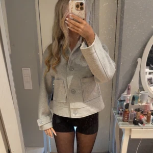 Ljusgrå ulljacka med stora knappar - Snygg ljusgrå jacka i ull med stora knappar framtill och två fickor. Jackan har en rak,passform och klassisk krage. Perfekt för dig som gillar stilrena och minimalistiska plagg.