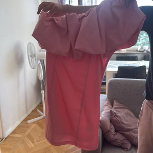 Rosa offshoulder kortklänning - Säljer en superfin rosa kortklänning med offshoulder och stor volang upptill. Klänningen har en figurnära passform och dragkedja i sidan. Perfekt för dig som vill sticka ut med en cool och feminin look. Materialet känns lätt och passar bra till varmare dagar. Jag säljer den då jag inte använt den på ett tag. Använt en gång och köpt ifrån H&M. Tveka inte o fråga🩷