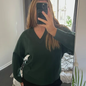 Mörkgrön v-ringad tröja från Wera - Mörkgrön v-ringad stickad tröja från Wera. Tröjan har en avslappnad passform med långa ärmar och ribbade muddar vid ärmslut och nederkant.