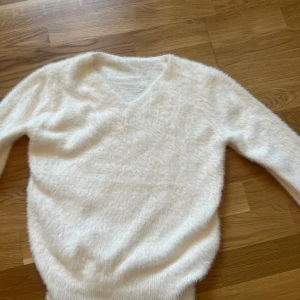 Vit fluffig stickad tröja v-ringad - Supermjuk och fluffig vit stickad tröja med v-ringning och långa ärmar. Perfekt för dig som gillar en cozy vibe och vill ha något stilrent men ändå mysigt. Passar till allt och är lätt att matcha med jeans eller kjol.