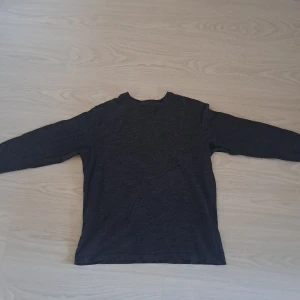 Mörkgrå långärmad tröja Polo Ralph Lauren - Mörkgrå långärmad tröja från Polo Ralph Lauren med klassisk rund hals och broderad rosa logga på bröstet. Tröjan är i mjuk bomull och har en clean, stilren look som passar perfekt till jeans eller chinos.