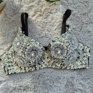 Glittrig paljett korsett-topp/bh - Säljer en svart korsett-topp/bh täckt med silvriga paljetter och stora glittrande stenar i blommönster. Justerbara axelband och hakknäppning bak. Avtagbara band. Storlek 32/70A. Aldrig använd.