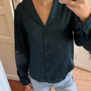 Mörkgrön satinblus från MSCH  - Snygg mörkgrön skjorta från MSCH Copenhagen i glansigt satinliknande material. Klassisk krage, knäppning framtill och långa ärmar. Färgen är mer emerald grön än vad som syns på bilderna. Lite trådar som slitits vid ärmarna som syns på bilderna.