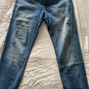 Tapered/mike jeans W34 L34 - Snygga blå jeans från Jack & Jones med klassisk design och ljusa slitningar framtill. Jeansen har normal passform och raka ben, tillverkade i mjukt denimtyg med skinnpatch bak i midjan så att de är mer hållbara vid alla typer av dagar. Perfekta för en avslappnad och trendig look. Helt nya som passar med allt dock har jag vuxit ur de. De är stretchiga och har en fin passform vid smalbenen och lite loose vid foten. Inga skambud!