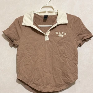 T-shirt ifrån Dazy - Snygg brun topp från Dazy med kontrasterande vit krage och knappdetalj framtill. 