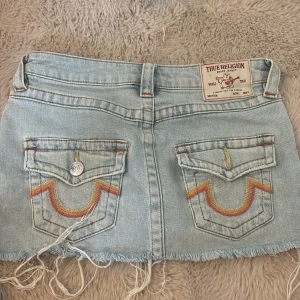 True Religion Sadie jeanskjol ljusblå - Jättebra skick Ljusblå kort jeanskjol från True Religion, modell Sadie Mini Skirt. Kjolen har fransad nederkant, klassiska jeansfickor med broderade detaljer i rött och gult,.jätte trendig över socialamedia och bra pris storlek 23