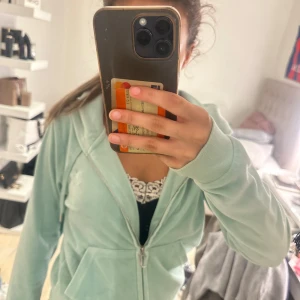 Mintgrön Juicy Couture hoodie i velour - Superfin mintgrön hoodie från Juicy Couture i mjuk velour. Klassisk modell med dragkedja, huva och fickor framtill. Perfekt för dig som vill ha en chill och trendig look. Snygg att matcha med jeans eller mjukisbyxor.