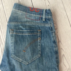 Dondup George skinny jeans blå - Snygga blå jeans från Dondup, modell George Skinny Fit. Jeansen har klassisk femficksdesign, knäppning med tre knappar och coola slitningar på låren och knäna. Tillverkade i mjukt denimtyg med en smal passform.