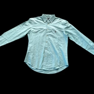 Ljusblå skjorta Polo Ralph Lauren L - Turkos Slim fit skjorta från Ralph Lauren 👔  Skick 6.5/10 nån fläck på ena ärmen och pytteliten över bröstet som syns på bilderna. Storlek L slim fit Pris går att diskutera 🤝 Hör av er vid frågor eller fler bilder :)
