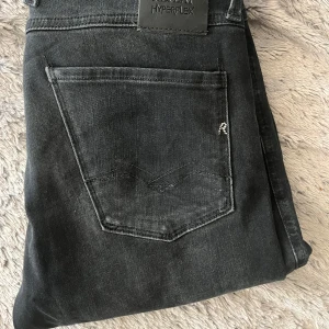 Svarta Replay Anbass Hyperflex jeans - Säljer ett par svarta Replay Anbass Hyperflex jeans med slim fit. Jeansen har klassisk femficksdesign, snygga detaljer och är tillverkade i stretchigt jeansmaterial för extra komfort. Perfekta för dig som gillar en smalare passform och stilren look.