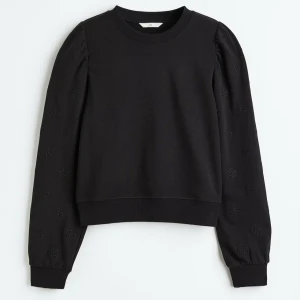 Svart sweatshirt med broderade ärmar - Svart sweatshirt med rund hals och långa ärmar. Ärmarna har broderade detaljer i form av små blommor och lätt puff vid axlarna. Tröjan har ribbade muddar vid ärmslut och nederkant. Perfekt för dig som gillar en enkel men ändå unik look.