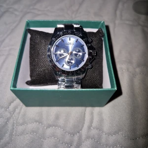 Hugo boss klocka - (Utan boxen) Stilren klocka med rund urtavla och länkarmband i blankt silverfärgat stål. Urtavlan har tydliga markeringar och flera knappar på sidan för extra funktioner. Perfekt för dig som gillar en clean och tidlös look.