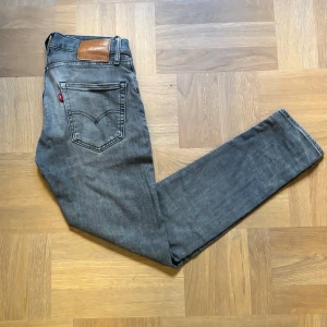  Gråa Levi's 512  - Snygga grå Levi's 512 jeans med klassisk femficksdesign och smal passform. Jeansen har en mörkgrå tvätt, raka ben och ikonisk läderpatch bak i midjan. Perfekta för dig som gillar en modern och stilren look. Storlek W30 L32. Byten kan även var aktuellt.