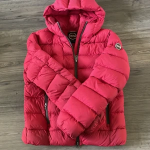 Röd pufferjacka från Colmar - Säljer en riktigt snygg röd pufferjacka från Colmar med huva och dragkedja framtill. Jackan har snygg design, två fickor med dragkedja och k Colmar-logga på ärmen. Perfekt för kalla dagar när du vill hålla stilen. En liten söm som har släppt, kan ses på bild 3 men i övrigt väldigt bra skick. Stl 46, nypris ca 3000, mitt pris 599 men det är även diskuterbart.