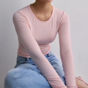Ljusrosa långärmad gina - Säljer en ljusrosa långärmad croppad topp i stretchigt och glansigt material. Toppen har en rund halsringning och sitter tight mot kroppen för en snygg siluett. Perfekt att styla med höga jeans eller kjol.