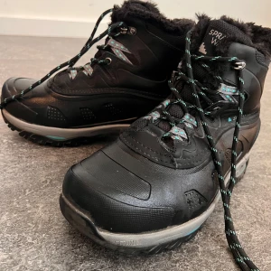Svarta vinterkängor från Sprayway - Svarta kängor från Sprayway med robust sula och snörning. Skorna har mjukt foder i pälsimitation och detaljer i turkos och grått på snörningen. Perfekta för kalla dagar med slitstark ovandel och extra grepp i sulan. Priset kan diskuteras. 