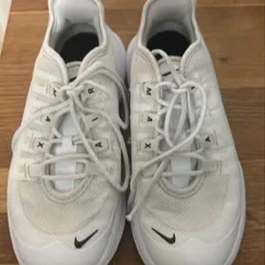 Nike Air Max vita sneakers - Fräscha vita Nike Air Max sneakers med svart swoosh på sidan och framtill. Skorna har snörning och en rund tå, samt en platt sula med tydligt Air Max-mönster undertill. Ovandelen är i mesh och syntet för skön ventilation och lätt känsla. Perfekta för dig som gillar sportig stil.