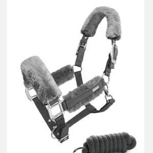 Grå fluffig grimma  - Säljer en grå grimma från Equestrian stockholm med mjuk, fluffig fuskpäls på nos, nacke och sidor. Grimman har silvriga spännen och en liten blå ängel-berlock. Perfekt för att ge hästen extra komfort och stil i stallet. Grimma, grimskaft och lyckoängel ingår, storlek COB