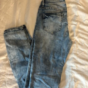 Ljusblå slitna jeans med skinny fit - Säljer ett par ljusblå jeans med skinny passform och slitna detaljer på benen. Jeansen har klassisk femficksdesign, dragkedja och knapp i midjan. Perfekta för en avslappnad och trendig look.