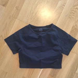Svart  croppad träningstopp M/L - Snygg svart croppad topp med korta ärmar och rund hals. Perfekt för träning eller sportiga outfits. Toppen har meshdetaljer på sidorna för extra ventilation och en tight passform som sitter skönt på kroppen.