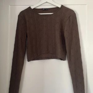 Brun croppad topp från Zara - Säljer en brun croppad topp från Zara med lång ärm och unik struktur i tyget. Toppen har rund halsringning och ett diskret mönster som ger en cool textur. Använd Max 2 gånger 