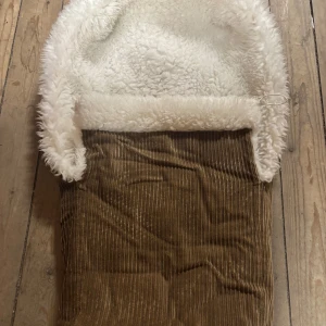 FIN VARM BarnvagnS sovsäck  manchester med  FÅR ULL JÄTTEBRA  - 🤗Säljer en beige åkdäck i manchester med mysigt vitt fårull.  Sovsäcken har breda ränder i tyget och en klassisk, lite retro look. Perfekt för  barnvagnen för en sovande bebis i vinter . Mått längd ca89CM BRED: 67cm🥰