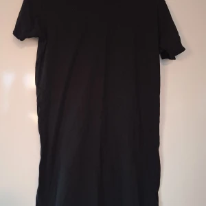 Svart basic lång t-shirt i bomull S/M - Enkel svart lång t-shirt i mjuk bomull med klassisk passform och korta ärmar. Perfekt att matcha med jeans eller shorts för en clean och stilren look.