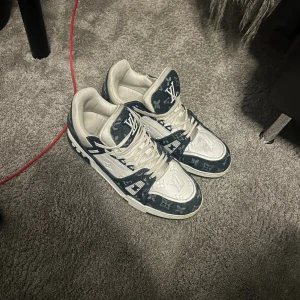 Louis Vuitton blåvita sneakers monogram - Säljer ett par Louis Vuitton sneakers i blått och vitt med klassiskt monogrammönster. Skorna har snörning, rund tå och platt sula. Materialmix av skinn och textil med tydliga LV-loggor på tunga och sidor. Riktigt snygga och unika sneakers för dig som vill sticka ut.