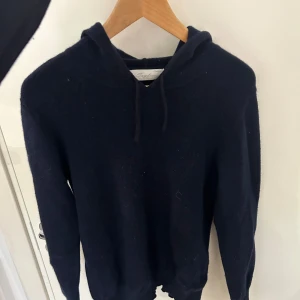 Mörkblå hoodie från Sayless - Mysig mörkblå hoodie från Sayless med huva och dragsko. Tröjan är stickad och har långa ärmar, perfekt för kyliga dagar. Enkel och stilren design som funkar till många outfits. Litet hål i armhålan som syns på bild 2, inget man som syns eller som man tänker på vid användning. Storlek S passar xs 